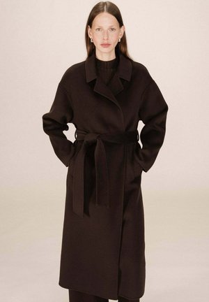 Manteau ceinturé marron foncé en tissu doux avec un grand col, des manches longues et des poches latérales, présentant une coupe droite et un design minimal.