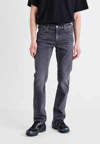 Jean en denim gris avec une coupe droite, comportant cinq poches, des passants de ceinture et un léger délavage. Associé à des baskets noires.