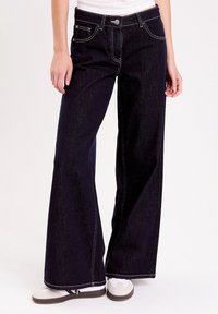Mørke denim brede ben jeans med hvid syning, fem lomme design og knaplukning. Har høj talje og afslappet pasform.