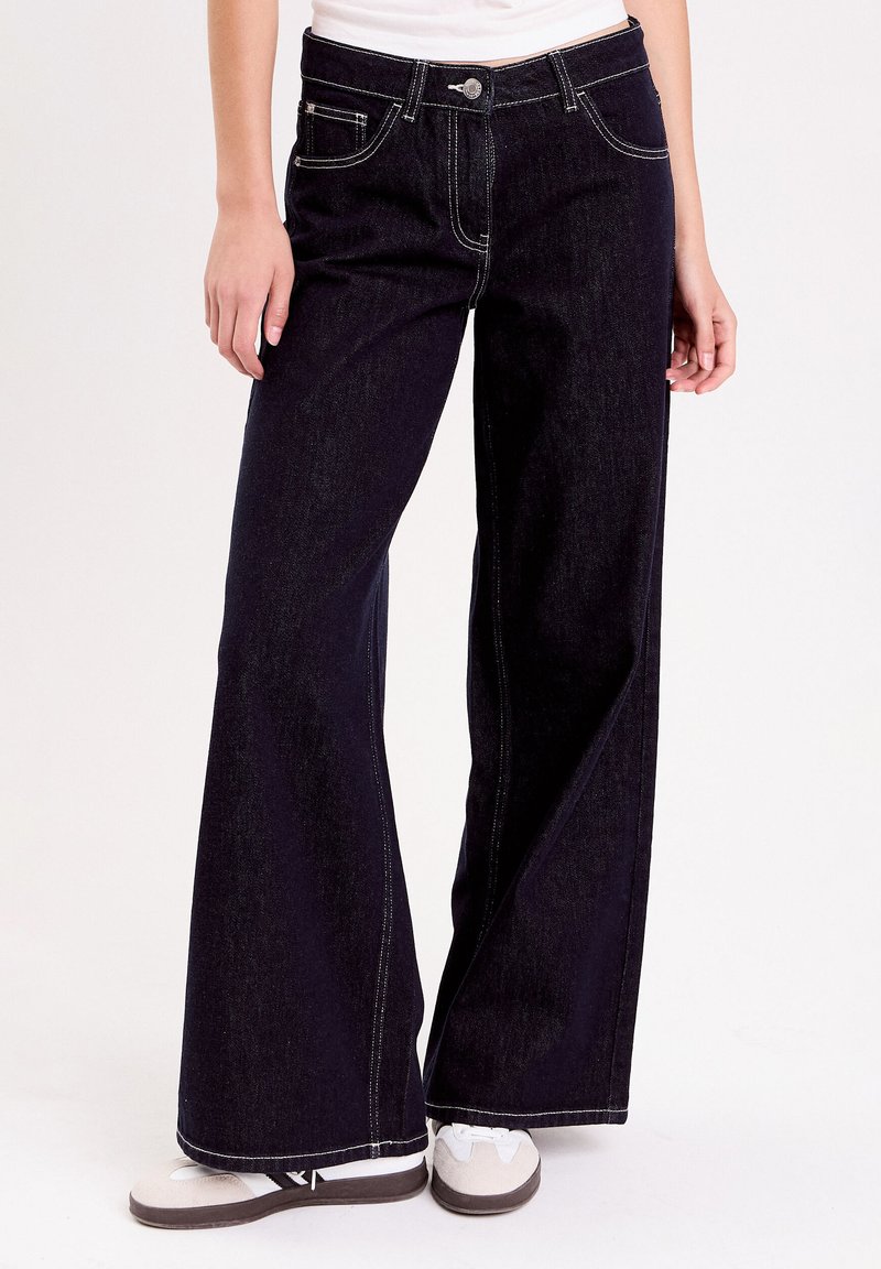 Mørke denim brede ben jeans med hvid syning, fem lomme design og knaplukning. Har høj talje og afslappet pasform.