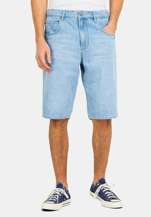 Hellblaue Denim-Shorts mit geradem Schnitt, fünf Taschen und einem Reißverschluss. Kombiniert mit navyblauen Turnschuhen aus Canvas.