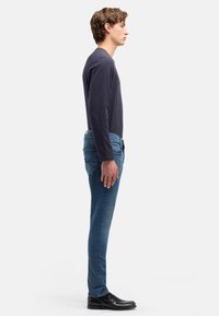 Granatowa koszula z długim rękawem, niebieskie dżinsy z denimu oraz czarne buty. Dżinsy mają dopasowany krój i lekkie przetarcia; koszula jest gładka i dopasowana.