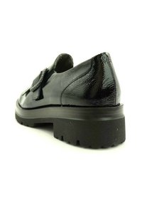 Zapato de cuero negro pulido con suela gruesa, punta redonda y acabado brillante. Presenta una correa decorativa en la parte superior.