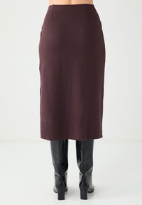 Burgundy midi skirt made of stretchy fabric with a fitted silhouette and side slits, paired with high black heeled boots.