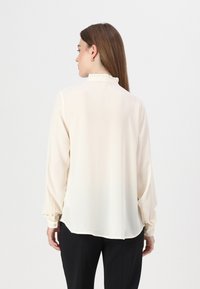 Crepe blouse in soft off-white with long sleeves, a ruffled collar, and button cuffs. Tailored fit with a slightly rounded hem.