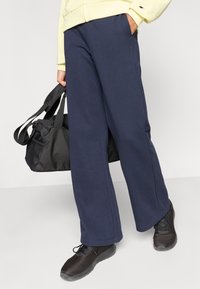 Σκούρο μπλε φόρμα από μαλακό ύφασμα, με άνετη εφαρμογή και πλαϊνές τσέπες. Συνδυασμένη με ανοιχτό κίτρινο φούτερ με κουκούλα και μαύρα παπούτσια.