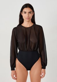 Mono negro con mangas largas transparentes, cuello redondo y cinturilla elástica, acompañado de un fondo de corte alto. Textura suave, diseño ajustado.