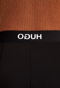 Leggings neri con una ampia vita elastica nera caratterizzata dal marchio bianco "HUGO". Il materiale è liscio con una finitura opaca.