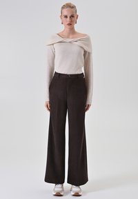 Top color beige chiaro a spalle scoperte con texture a maglia, abbinato a pantaloni ampi a vita alta di colore marrone scuro e sneaker bianche.