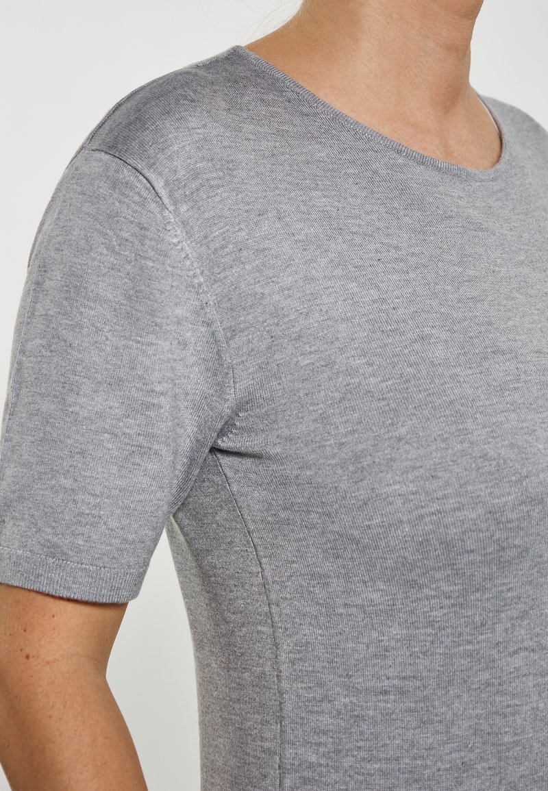 Tricou gri cu mânecă scurtă, dintr-un material moale, cu decolteu rotund și textură uniformă, având detalii de cusătură vizibile pe cusături.