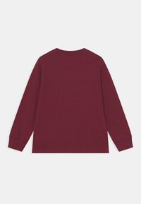 Camiseta de manga larga color burdeos, hecha de algodón suave, con cuello redondo y corte estándar, con puños acanalados y una textura suave.