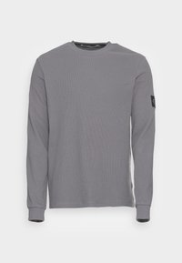Långärmad tröja med rund hals i grått våfflat tyg. Har en svart logotyp på vänster ärm. Regular fit och ribbade ärmslut.