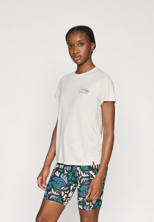 Világos bézs rövid ujjú póló apró grafikával; fekete, színes mintás kerékpáros rövidnadrág lombmotívummal.