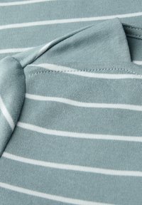 Helles Teal-Stoff mit weißen horizontalen Streifen. Nahaufnahme zeigt eine weiche Textur und Details des gefalteten Kragens. Die Nähte sind an den Kanten sichtbar.