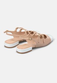 Zapatos slingback de charol beige con una punta blanca, que presentan un bajo tacón cuadrado y dos correas decorativas con hebillas doradas.