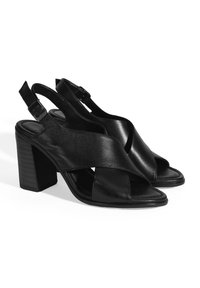 Zwarte leren slingback hakken met een blokhak, kruisbandontwerp en een gladde textuur. Verstelbare gespsluiting op de hak.