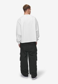 White long-sleeve shirt with a relaxed fit and dropped shoulders, paired with loose black cargo pants featuring side pockets.