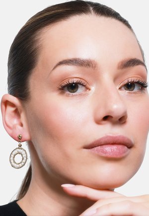 Goldene, kreisförmige Ohrringe mit einem strukturierten äußeren Ring und einem glatten inneren Kreis, die ein hängendes Design aufweisen und mit einem kleinen goldenen Ball befestigt sind.