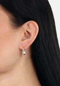 Pendientes de aro en tono dorado con un diseño retorcido y cristales transparentes incrustados a un lado. Acabado elegante y pulido.
