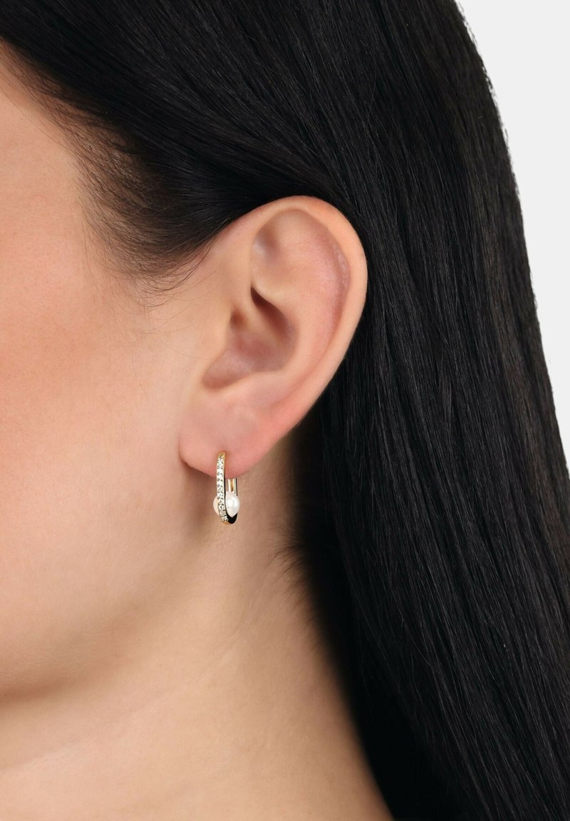 Pendientes de aro en tono dorado con un diseño retorcido y cristales transparentes incrustados a un lado. Acabado elegante y pulido.
