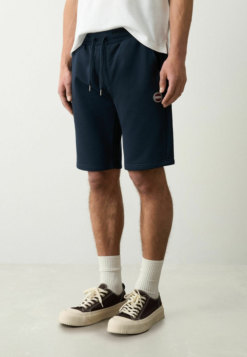 Shorts da uomo in blu navy realizzati in un materiale morbido, con vita elastica e cordino, caratterizzati da una piccola etichetta con logo sul lato sinistro.