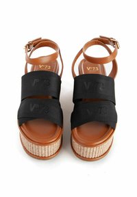 Sandali platform marroni con due cinghie elastiche nere che presentano un logo. La suola intermedia con texture in rattan aggiunge altezza e contrasto alla pelle liscia.