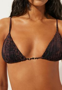 Černý a hnědý bikiny vršek ve tvaru trojúhelníku s řasitou látkou, s tenkými ramínky a zlatavým kováním uprostřed.