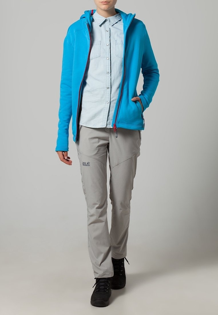 Blauwe fleece hoodie met een volledige rits, gecombineerd met een lichtblauw button-up shirt en lichtgrijze broek. Zwarte wandelschoenen maken de outfit compleet.