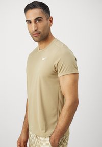 Beige trenings t-skjorte med rund hals og korte ermer, med en liten hvit Nike-logo på brystet og en glatt, tettsittende tekstur.