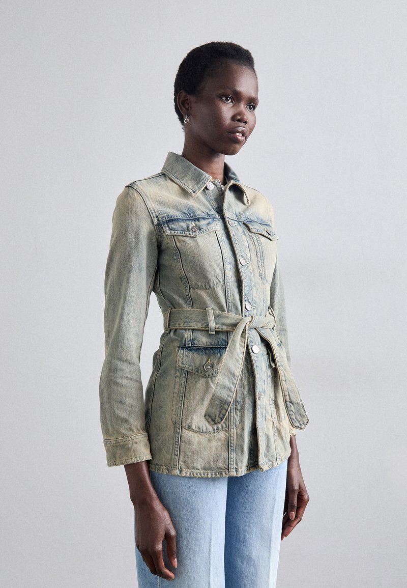 Hele sinine denim jakk kitsaste taljega, nööpidega ees, kahte rinna taskut ja pikad varrukad, vöödiga disain ja kulunud tekstuur.