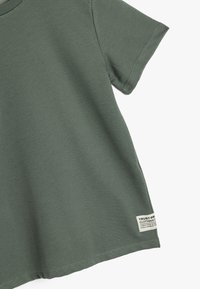 T-shirt a righe verde oliva con maniche corte, dotata di un piccolo etichetta rettangolare del marchio sul bordo inferiore e un design a taglio dritto.