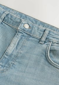 Jeans din denim de culoare albastră deschisă, cu fermoar la mijloc, închidere cu buton și design cu cinci buzunare, având detalii de cusătură contrastante.