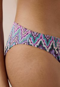 Bikiny s viacerými farbami s cik-cak vzorom v purpurovej, ružovej, zelenej a krémovej farbe. Materiál vyzerá hladko a elasticky.