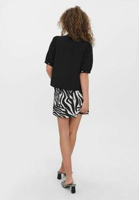 Blusa nera a maniche corte con vestibilità ampia, indossata su una gonna a motivo zebra. La modella indossa sandali con tacco verdi.