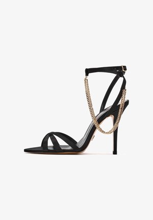Black stiletto sandal with multiple thin straps, a pointed toe, suede texture, and a gold chain accent on the ankle strap.