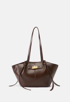 Borsa tote in pelle marrone con forma arrotondata, manici lunghi, un dettaglio hardware dorato sul davanti e lacci sui lati.