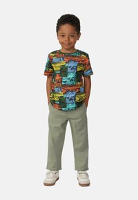 Korte mouwen T-shirt in levendige kleuren met een grafisch ontwerp van verschillende landschapsafdrukken, gecombineerd met lichtgroene broek en witte schoenen.