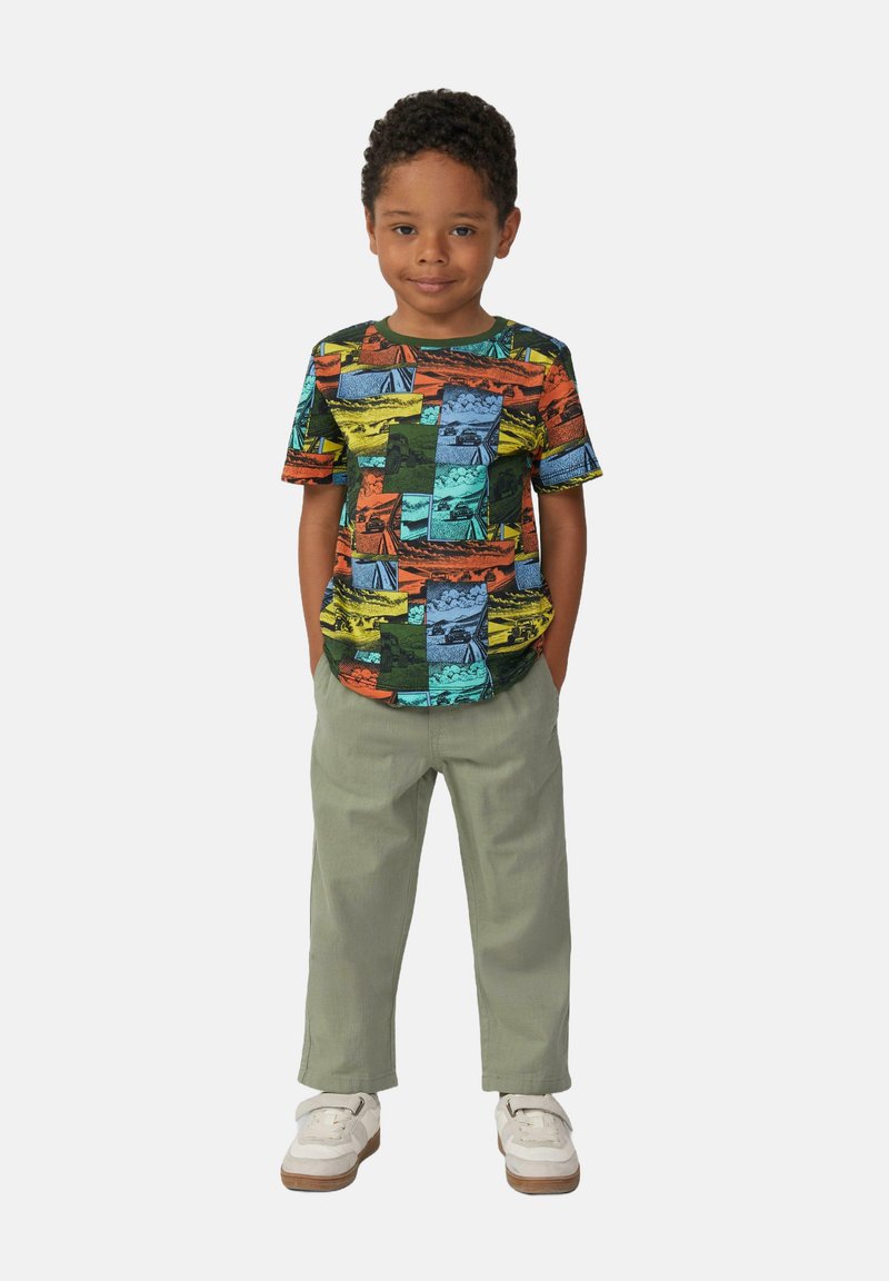 Korte mouwen T-shirt in levendige kleuren met een grafisch ontwerp van verschillende landschapsafdrukken, gecombineerd met lichtgroene broek en witte schoenen.