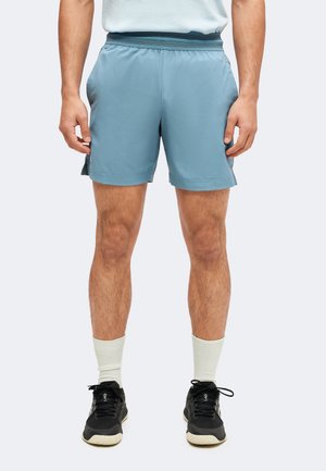 Man draagt lichtblauwe sportshorts, witte sportsokken en zwarte hardloopschoenen, staat met ontspannen handen langs het lichaam.