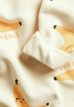 Zachte stof met speelse banaanillustraties, één banaan heeft een glimlachend gezicht met blozende wangen op een lichte crèmekleurige achtergrond.