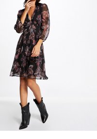 Sort, gennemsigtig kjole med blomster paisley-mønster, dyb V-hals og puffede ærmer. Kombineret med sorte, spidse ankelstøvler.