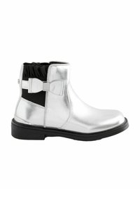Botines metálicos plateados con punta redonda, lados elásticos y un lazo negro como acento. Presenta un collar texturizado y una suela plana negra.