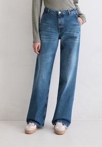 Brede blauwe denim jeans met een hoge taille, vijf zakken en een vervaagde wassing. Draagt het met witte sneakers met een tan platformzool.