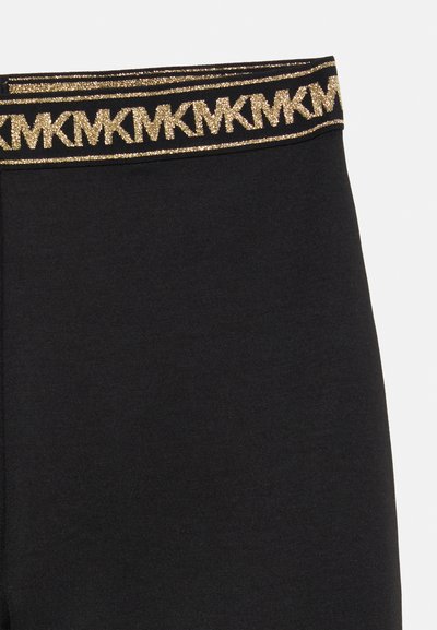 Juodos leggingai su minkšta tekstūra ir dekoratyvia auksine metaline juosta, turinčia kartotinį raidžių raštą.