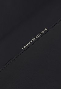 Crni kožni novčanik s zlatnim logotipom "TOMMY HILFIGER", minimalističkog dizajna sa glatkom teksturom i urednim šavovima duž rubova.