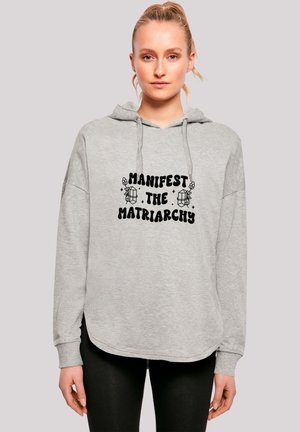 Grauer Hoodie mit lockerer Passform, der auf der Vorderseite einen schwarzen Aufdruck mit dem Slogan "Manifestiere die Matriarchat" und floralen Akzenten zeigt.