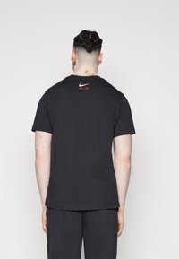 Svart bomullströja med korta ärmar och rundad halsringning. Har en vit Nike-logotyp och 'AIR' i rött, placerat på den övre ryggen.