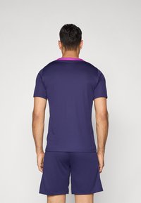 Purple athletic shirt with short sleeves and a round neckline, featuring a pink accent on the collar. Worn with matching shorts.