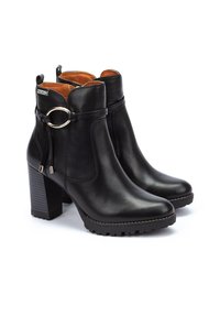Botas de tobillo de cuero negro con un tacón alto y cuadrado, cremallera lateral y un accesorio decorativo de hardware plateado en el tobillo. Textura suave con detalles de costura.