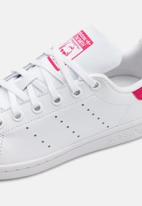 Vita lädersneaker med rosa detaljer, med en texturerad yta, rund tå och perforerade detaljer längs sidorna.